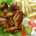 närbild av en portion gyros på kyckling, pommes frites, fetaost, tomat och inlagd gurka på salladsblad