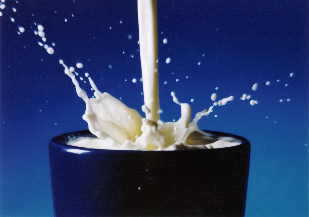 Mjölk som hälls upp i svart mugg med blå bakgrund