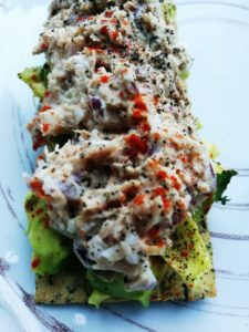 En knäckebit med avokado och tonfiskröra kryddad med paprika och svartpeppar tagen i närbild på en vit tallrik